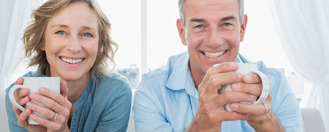 Smiling couple holding coffee mugs looking directly at camera