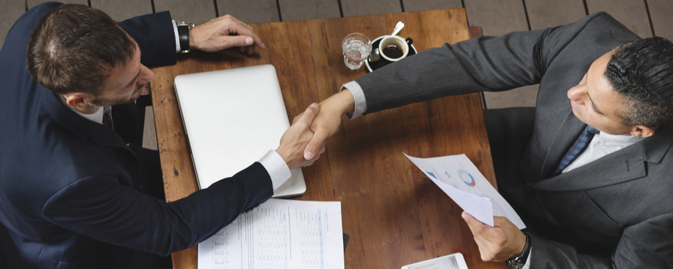 Business professional and customer shake hands over desk with papers and laptop around