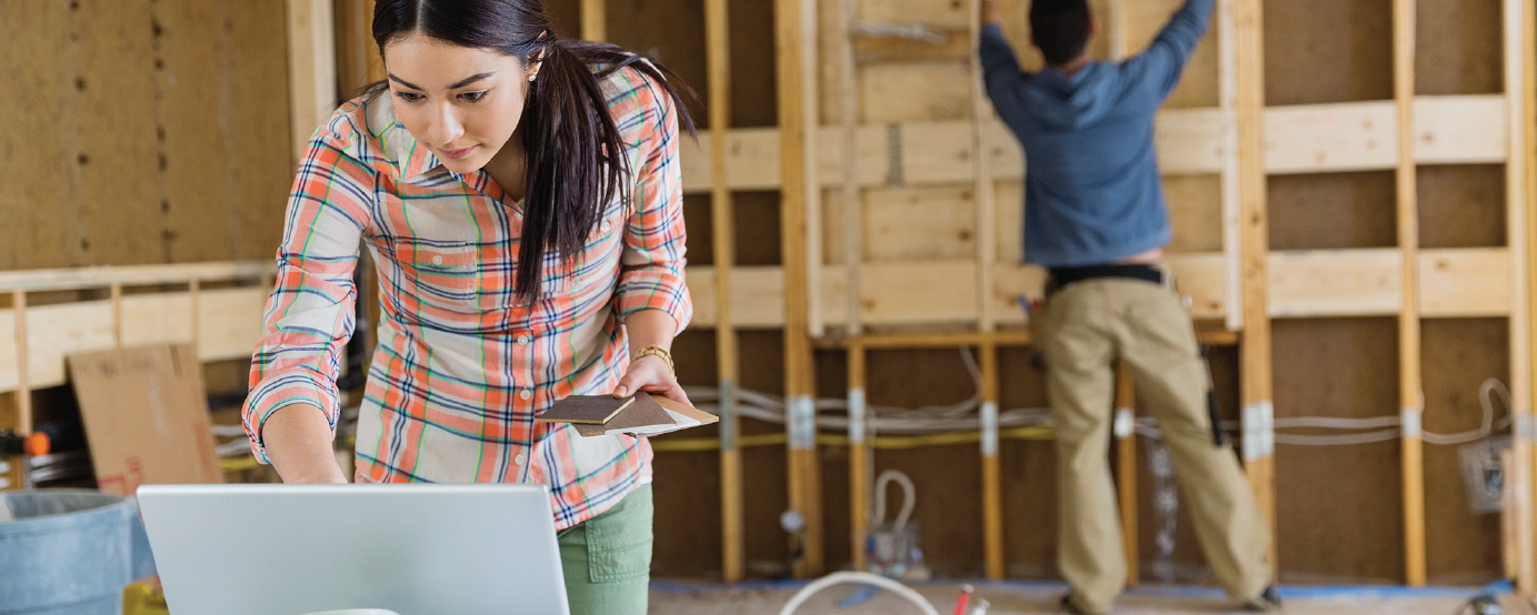 woman holding color samples and looking at her computer contractor blurred in background