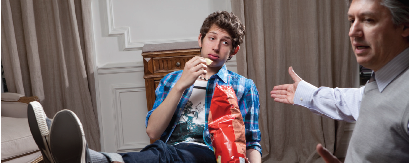 Teenager with bag of chips looking discourage as dad is pointing and looking away from teen