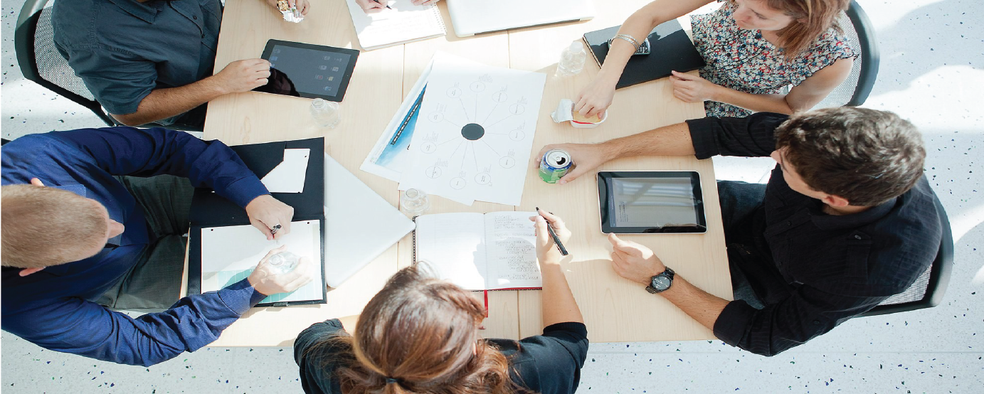 People sitting around table with laptops, papers, pens in discussion