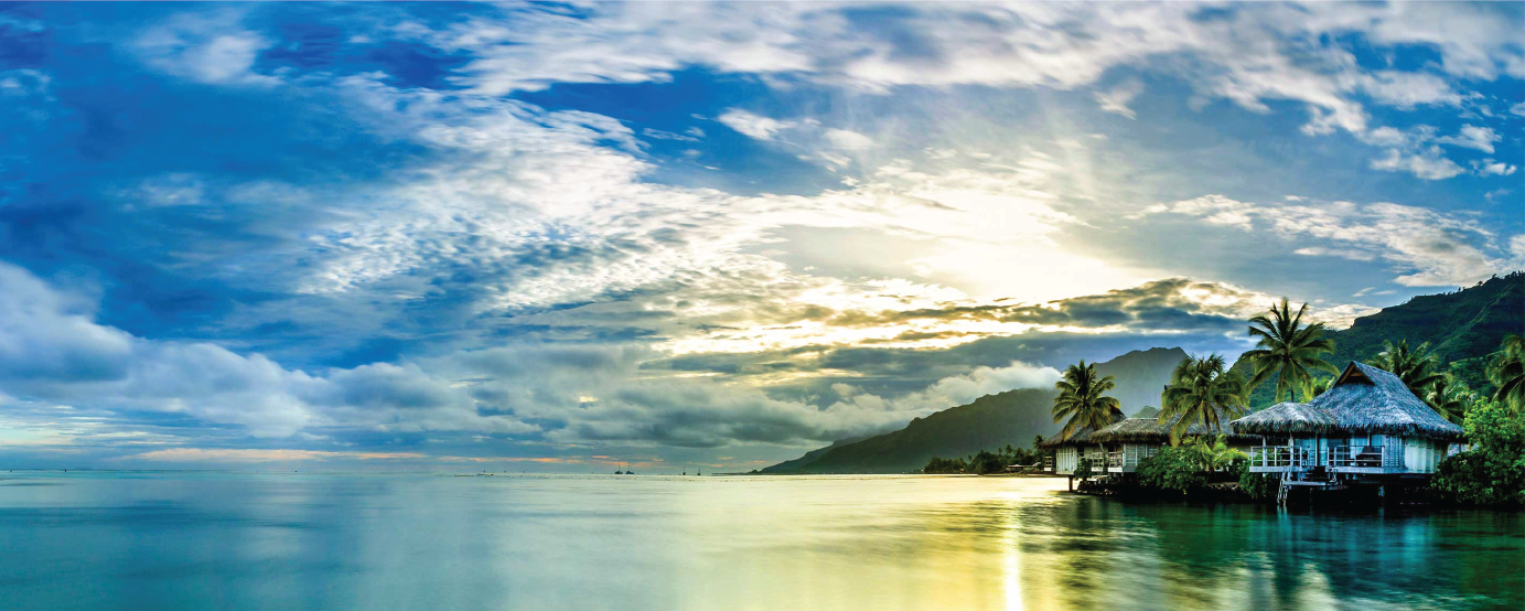 beautiful grass roofed cottage sits on beach with palm trees all around sun peeking through white puffy clouds