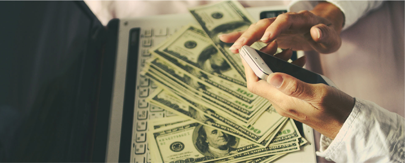 close up of woman's hands holding phone large money stack underneath