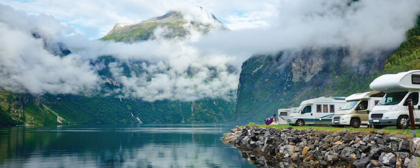 Line of RVs parked overlooking lake with green mountains with low hanging clouds in background