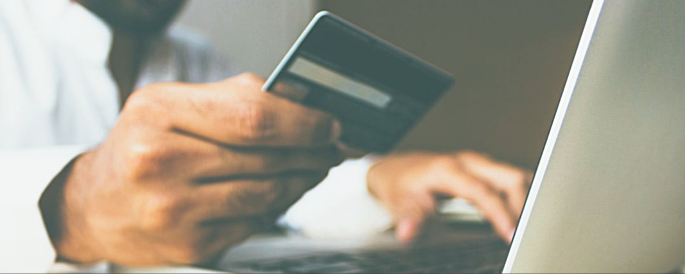 Close up of hand holding a credit card while the other hand types number into computer