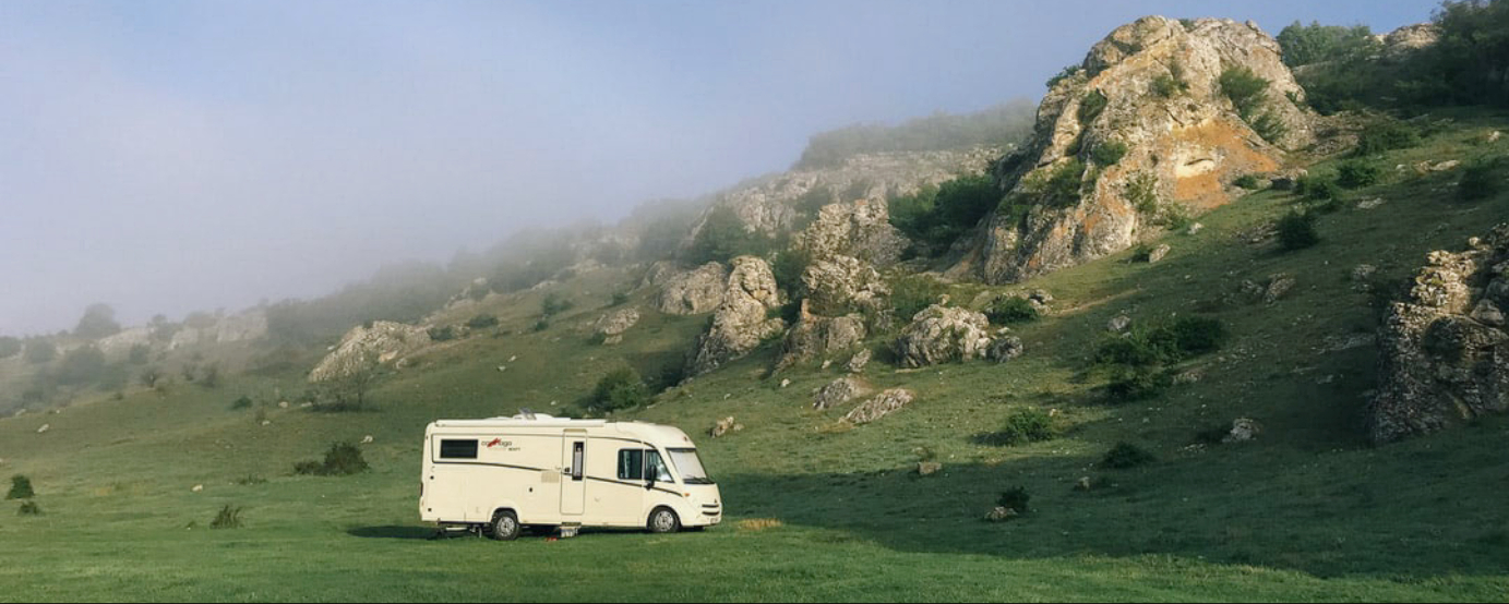 RV parked on grass and rocky mountains
