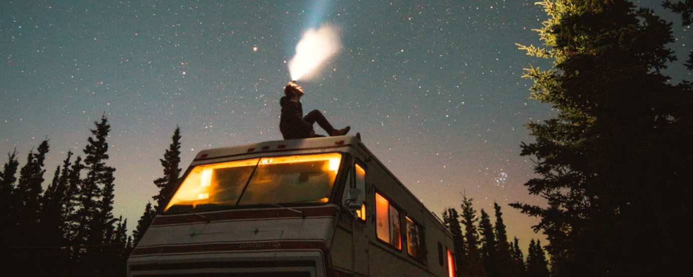 Man sitting on top of RV looking up at stars