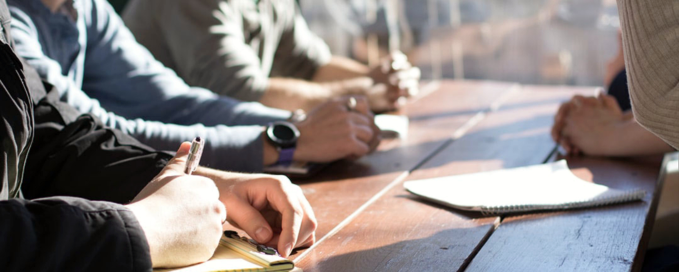 People gathered around a table, only their arms are visible, possibly interacting or sharing something.