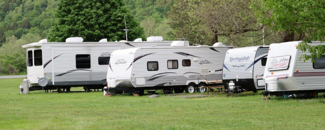 Photo of four towable RVs parked in grassy setting with green trees in background