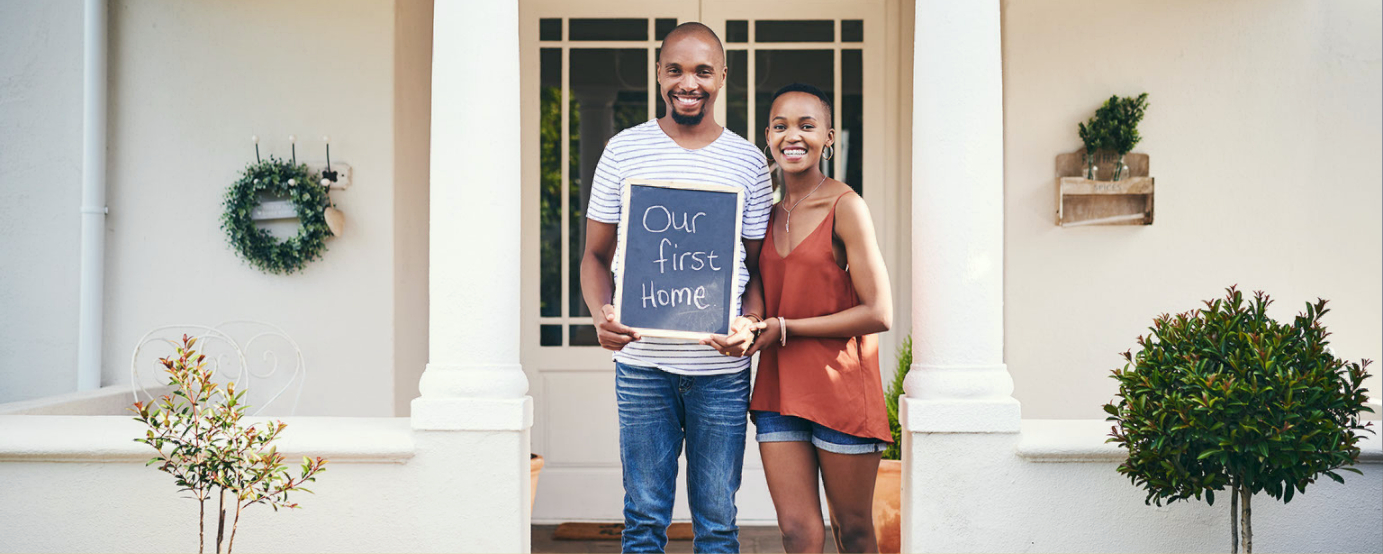 Young happy couple holding a chalkboard sign with the words Our First Home