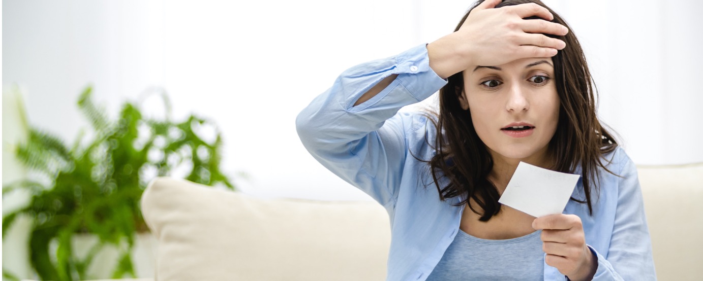 Confused and shocked woman's hand on her head looking at piece of paper she's holding