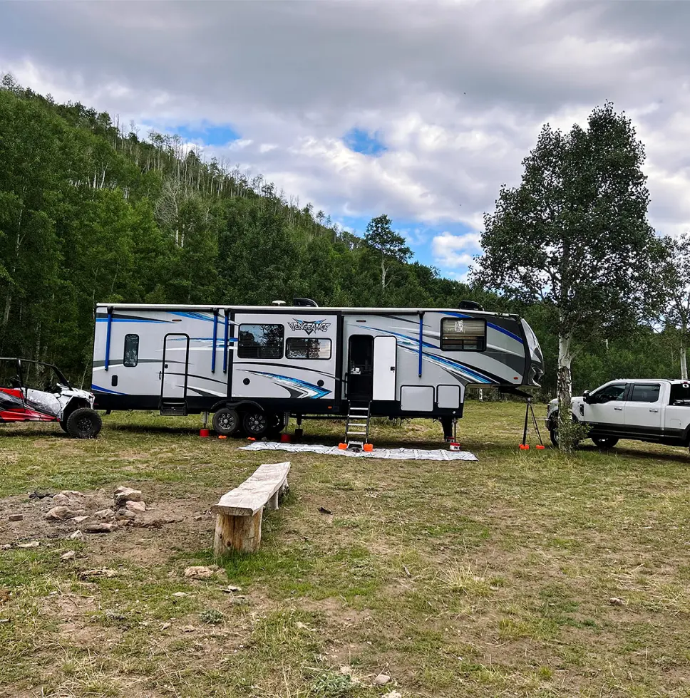 Photo of a mountain camp site showing a fifth wheel travel trailer, a side-by-side, and a truck.