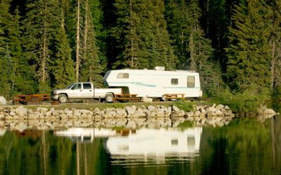 Picture of truck and RV with lake in forefront and trees in background.